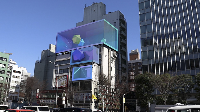ビルが並ぶ街並み。写真中央にそびえるビルの上に、大型該当ディスプレイが設置されている。画面には弊社が制作した3D広告動画が表示されている。